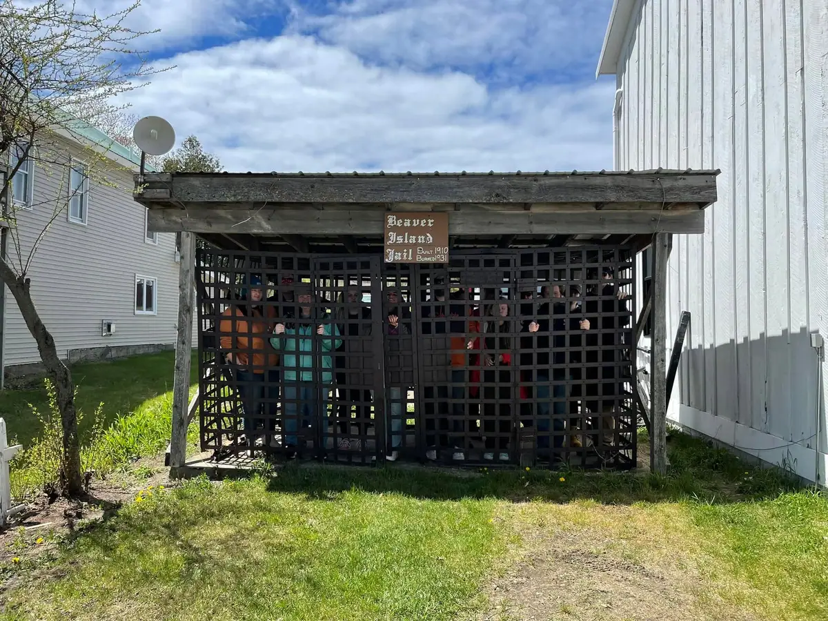 People pose behind the wooden bars of a small outdoor structure beneath a sign.
