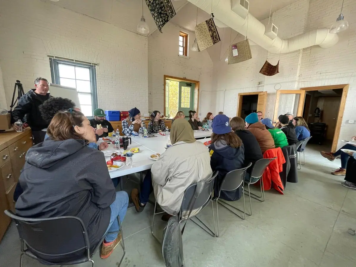 People share a meal around a long table in a bright white-brick room.