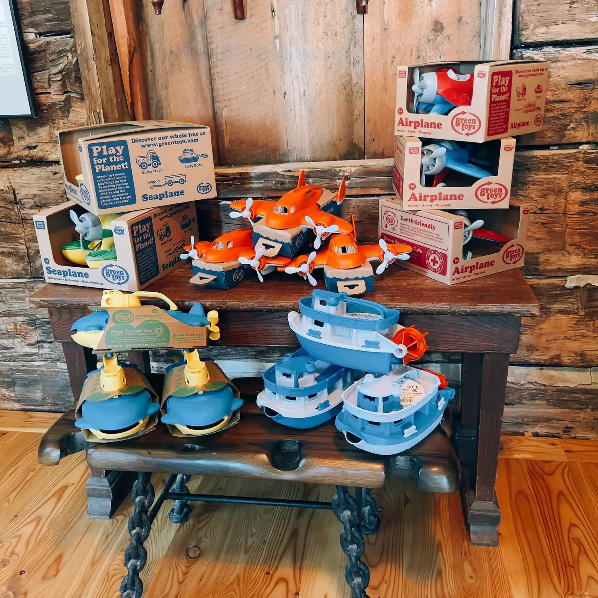 Toy airplanes, seaplanes, boats, and a dump truck arranged on a wooden bench.