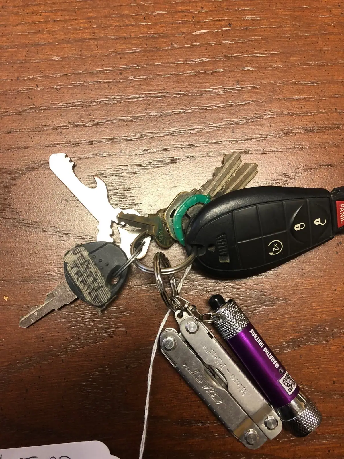 Keys, a black key fob, a multitool, and a purple flashlight lie on a wooden surface.