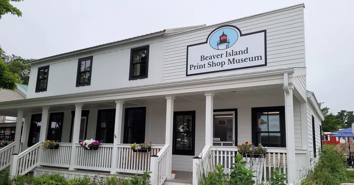 White wood-sided building with a covered porch, flower boxes, and a large museum sign bearing a lighthouse emblem.
