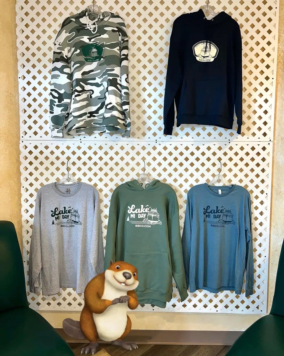 Five hooded and long-sleeved garments hang on a white lattice display above a plush beaver figure.