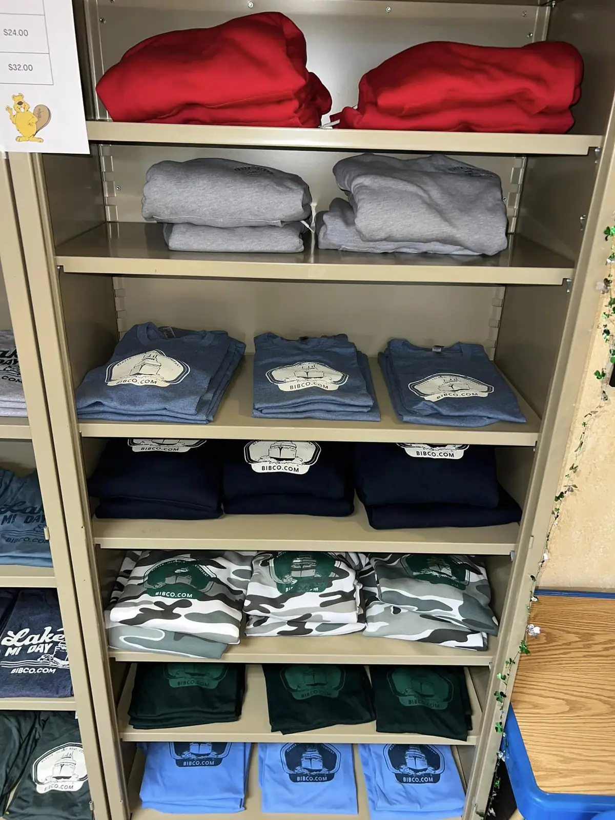 Shelves display folded red, gray, blue, navy, green, and camouflage clothing with printed logos.
