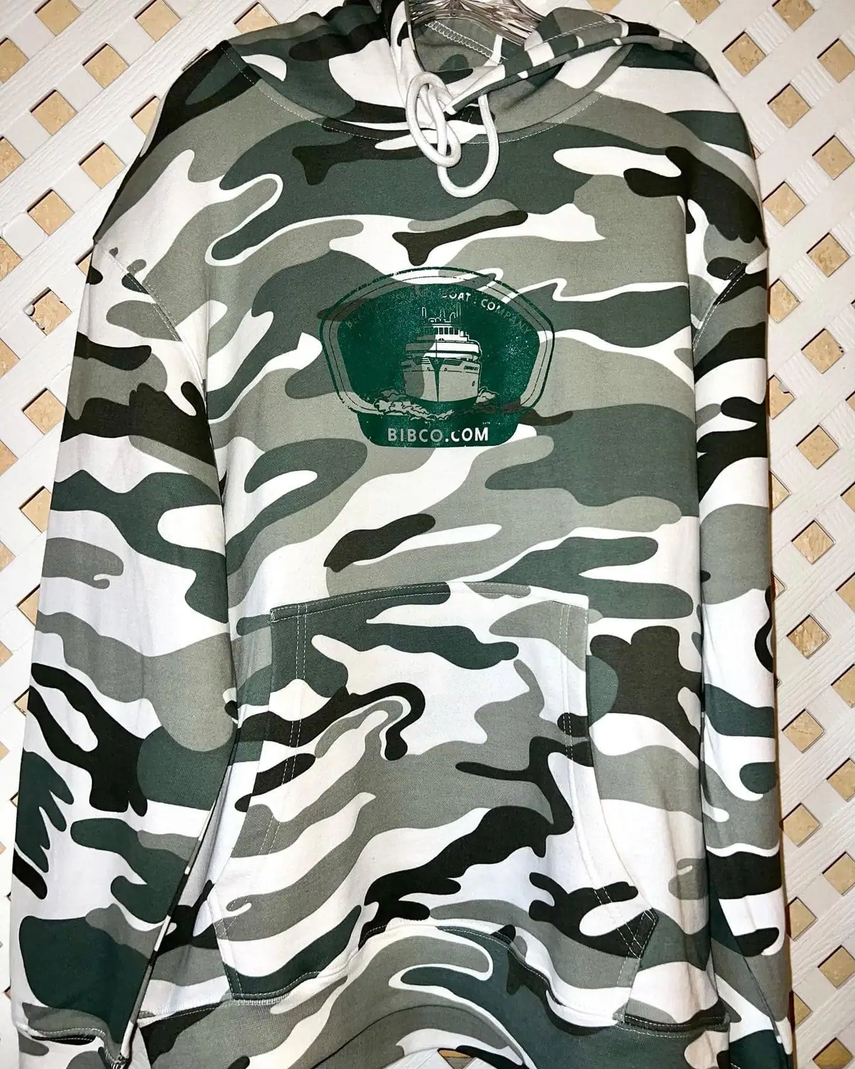 Camouflage hooded sweatshirt with a green boat-company emblem and website lettering.