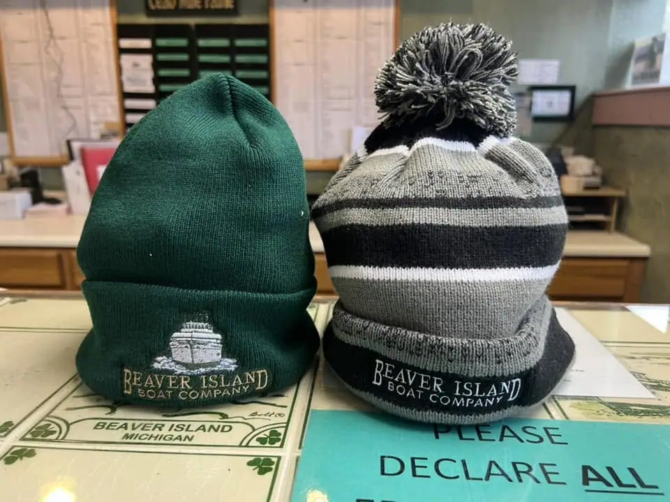 Two knitted boat-company hats displayed on a counter, with printed maps and a partial notice beneath them.