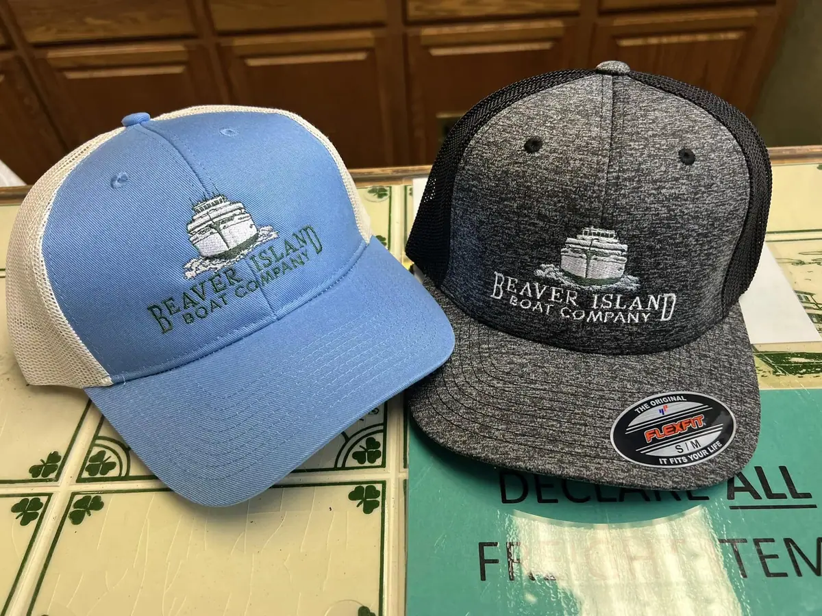 Two embroidered trucker caps with boat logos and company lettering rest on a printed tabletop.