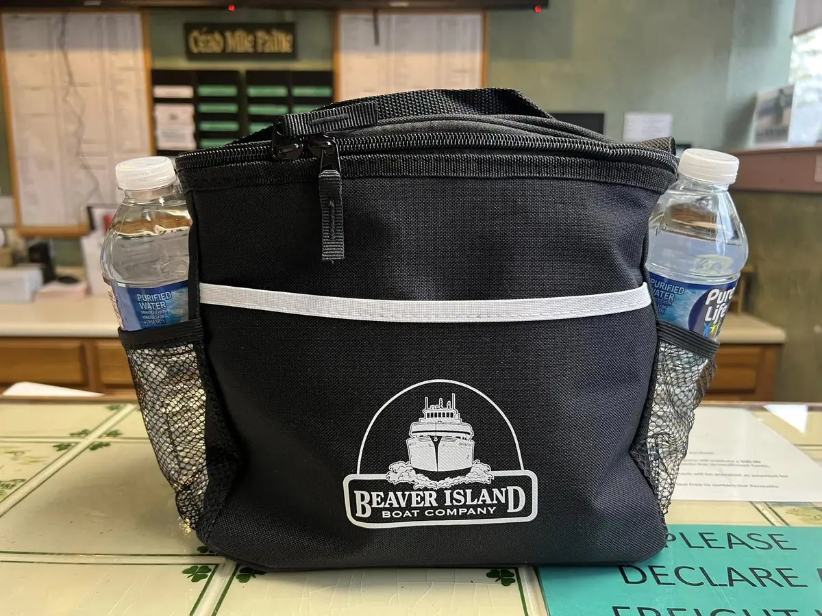 A black zippered bag with a vessel logo, two water bottles, and printed lettering sits on a patterned counter.