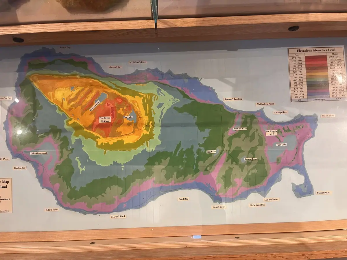 Color-coded relief map with labeled bays, lakes, points, and elevation bands, displayed in a wooden frame.