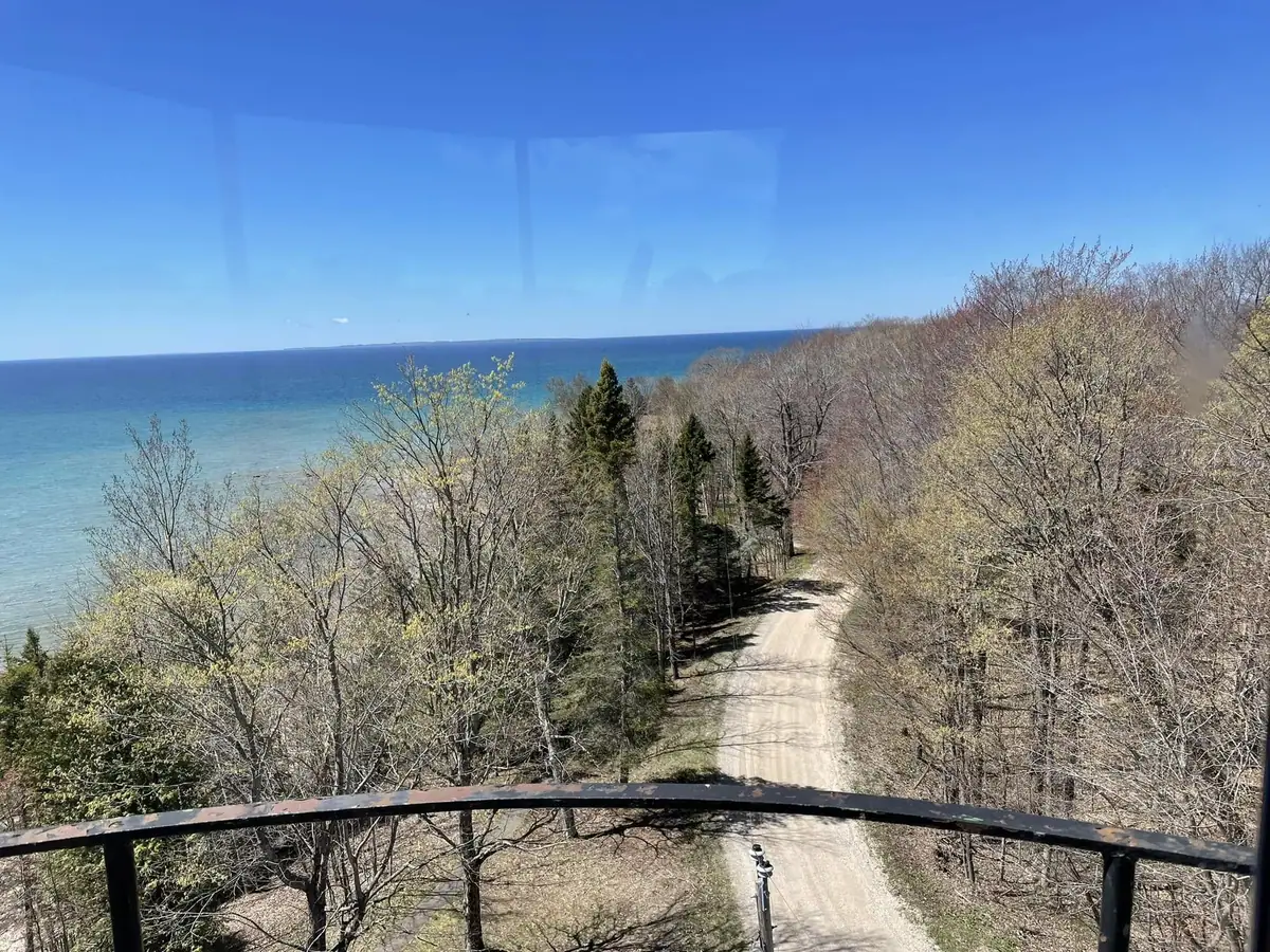 Elevated view over a wooded shoreline, dirt road, and expansive blue water.