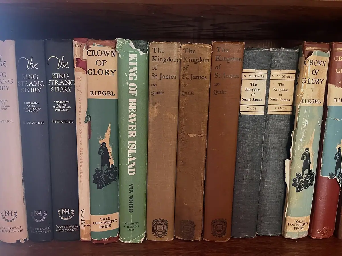 Close-up of a wooden bookshelf filled with worn books about religious and regional history.