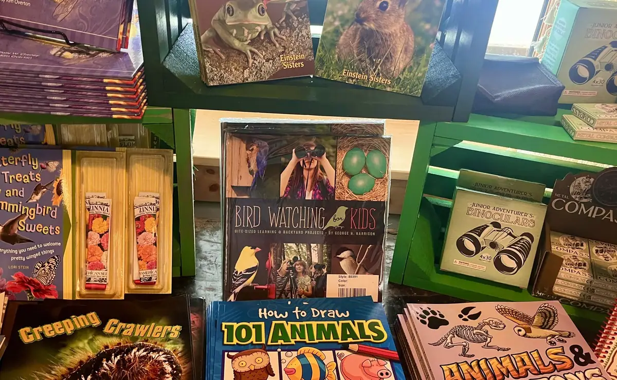 A shelf display of nature-themed books, binoculars, seed packets, and other educational materials.