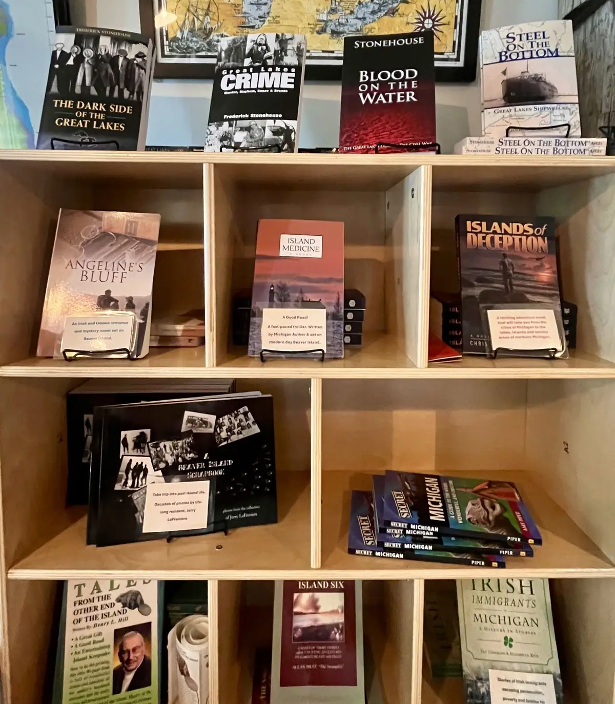 A wooden bookcase displays books, promotional cards, and a framed map-like image.