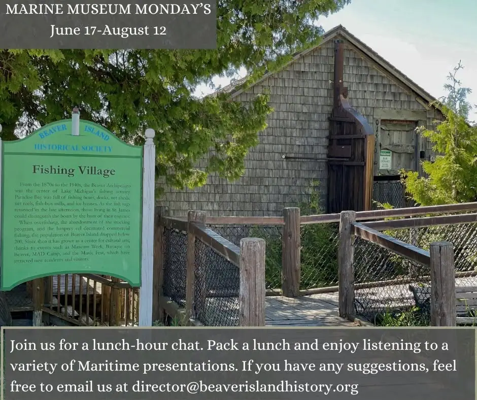 A shingled museum building, green interpretive sign, and fenced wooden walkway beneath trees.