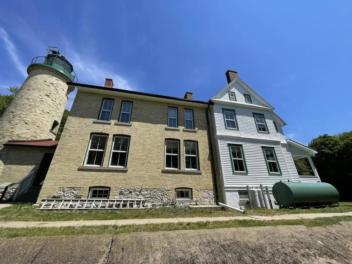 A brick lighthouse and adjoining buildings stand beneath a clear blue sky.
