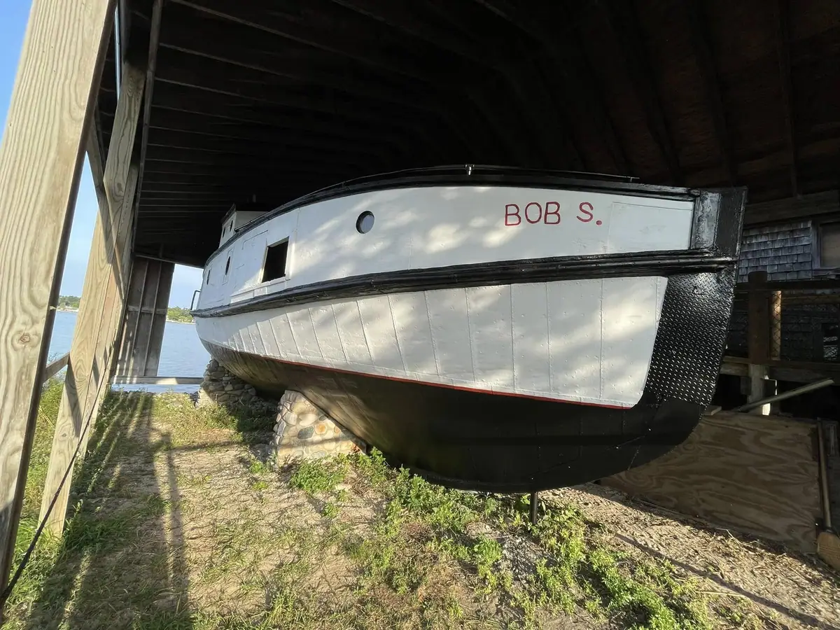 A white-and-black boat marked “BOB S.” rests on supports beneath a wooden shelter beside the water.
