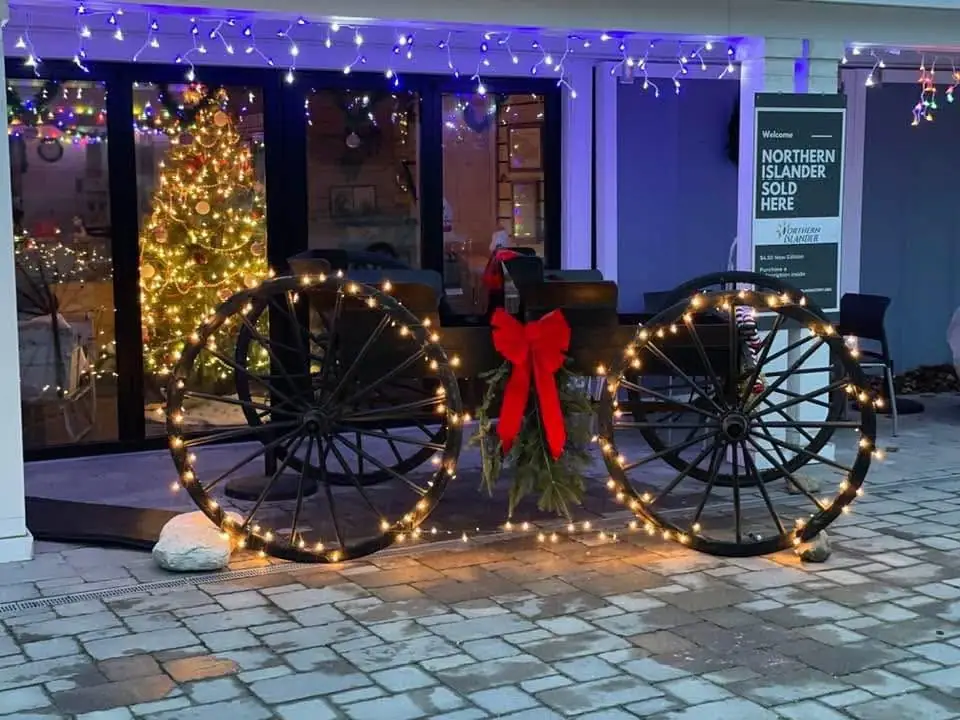 A storefront entrance decorated with lit wagon wheels, a red bow, greenery, and a Christmas tree.