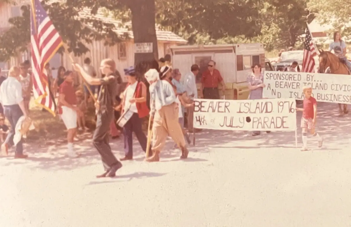 People walk in a parade past hand-lettered signs, American flags, and a mounted rider.