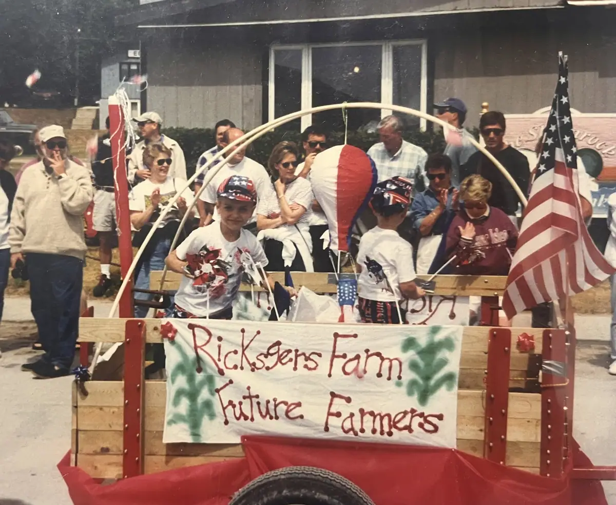 Children and adults ride a decorated parade float with flags and a banner reading “Ricksgers Farm Future Farmers.”
