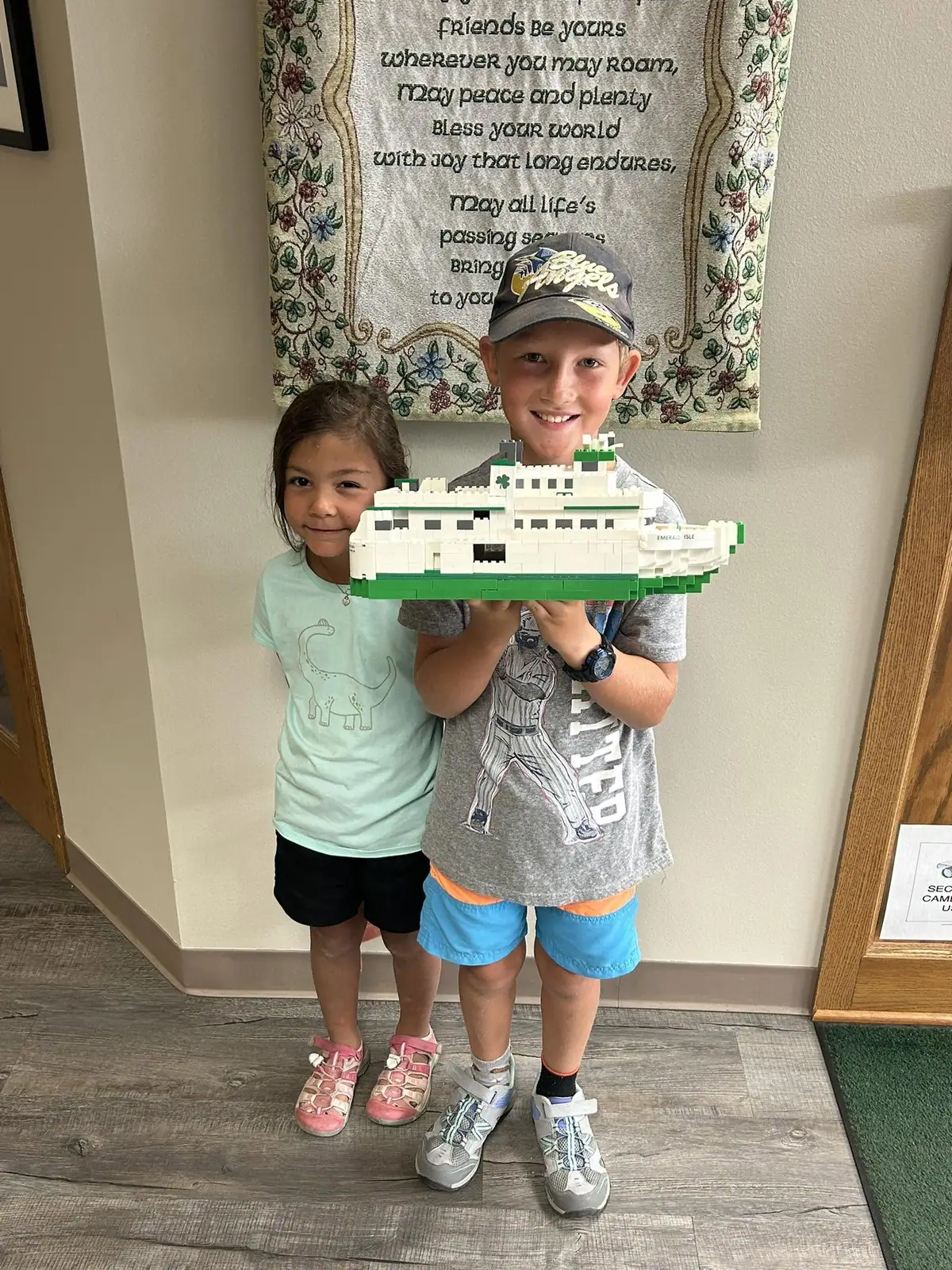 Two children hold a large white-and-green block-built ferry model indoors.