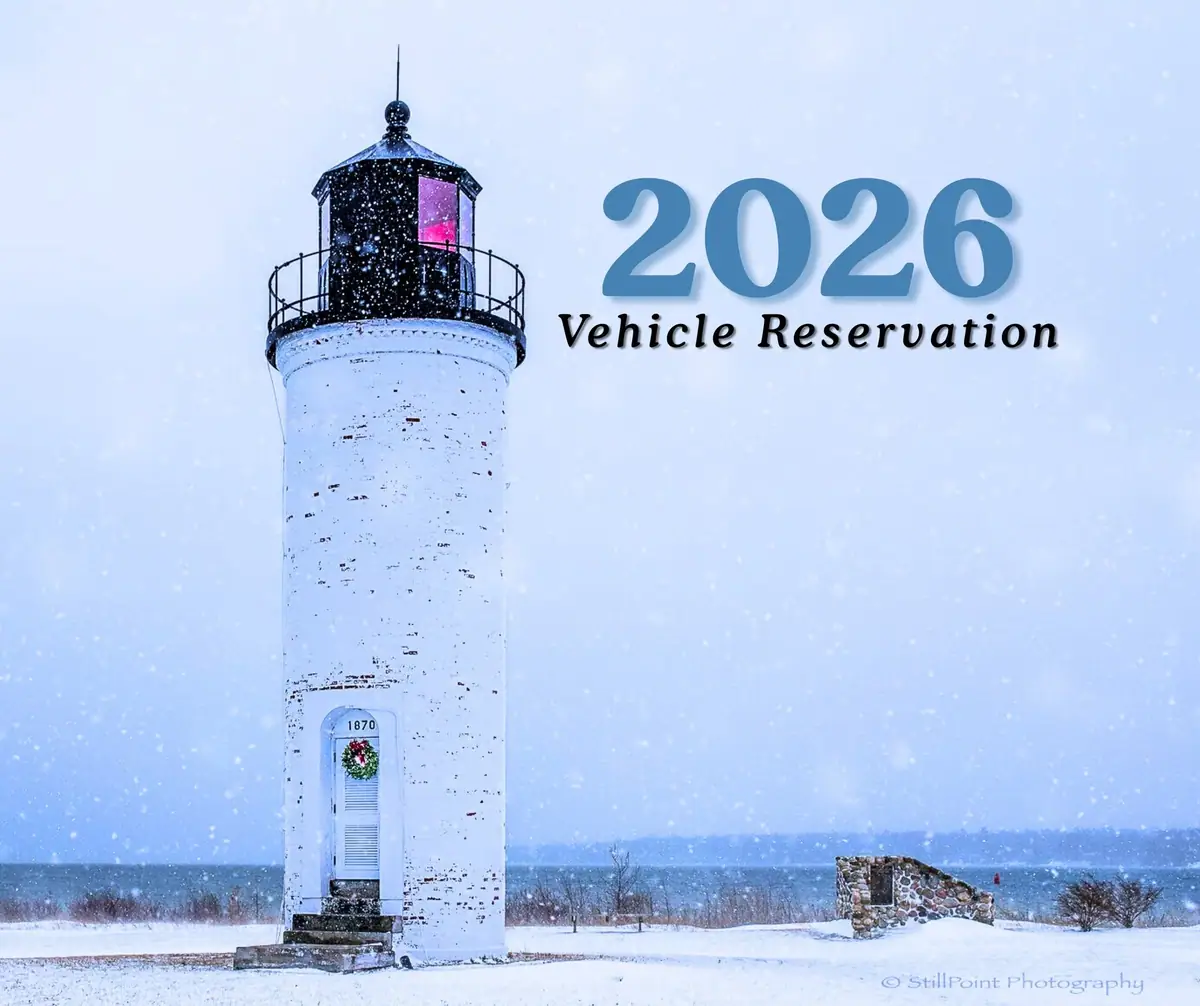 Snow-covered white lighthouse beside the water, with large “2026 Vehicle Reservation” lettering.