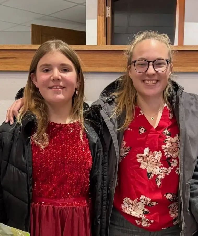 Two smiling people pose together indoors, wearing red clothing and dark outerwear.