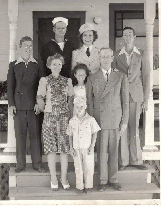 Black-and-white group portrait of seven adults and two children on the steps of a house porch.
