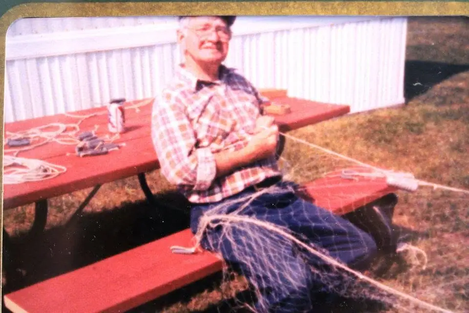 A man sits with folded arms on a red picnic table, surrounded by strands of artificial webbing.