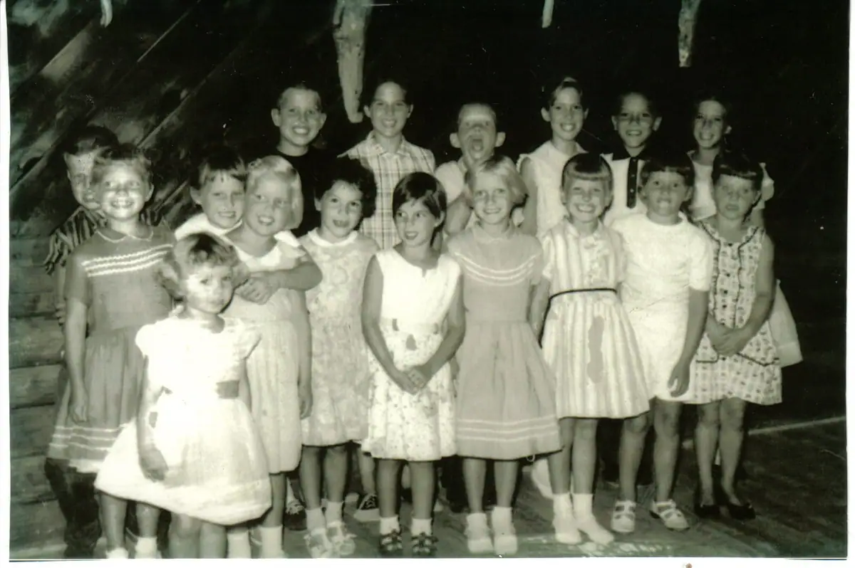 Seventeen children pose in rows inside a rustic wooden building.