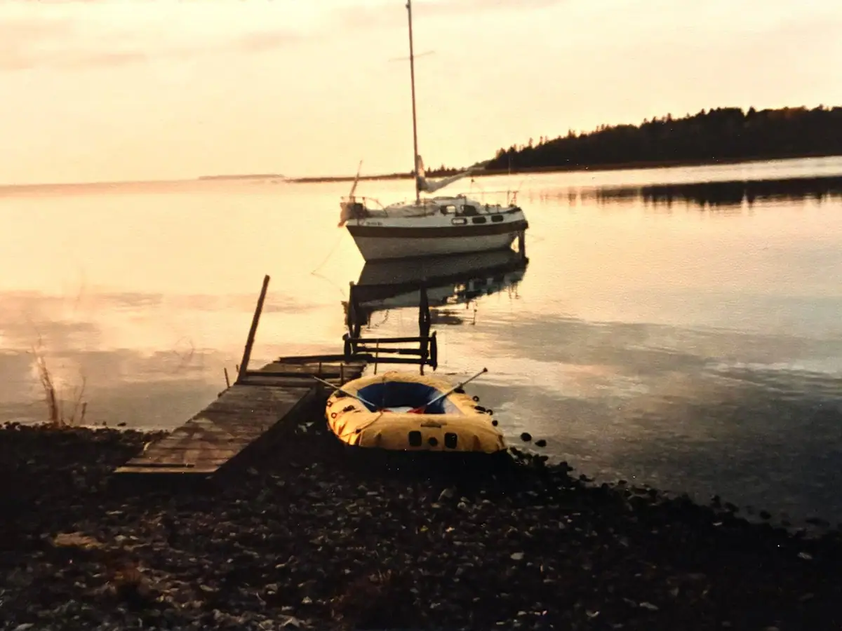 A sailboat and yellow inflatable dinghy beside a wooden dock in warm evening light.