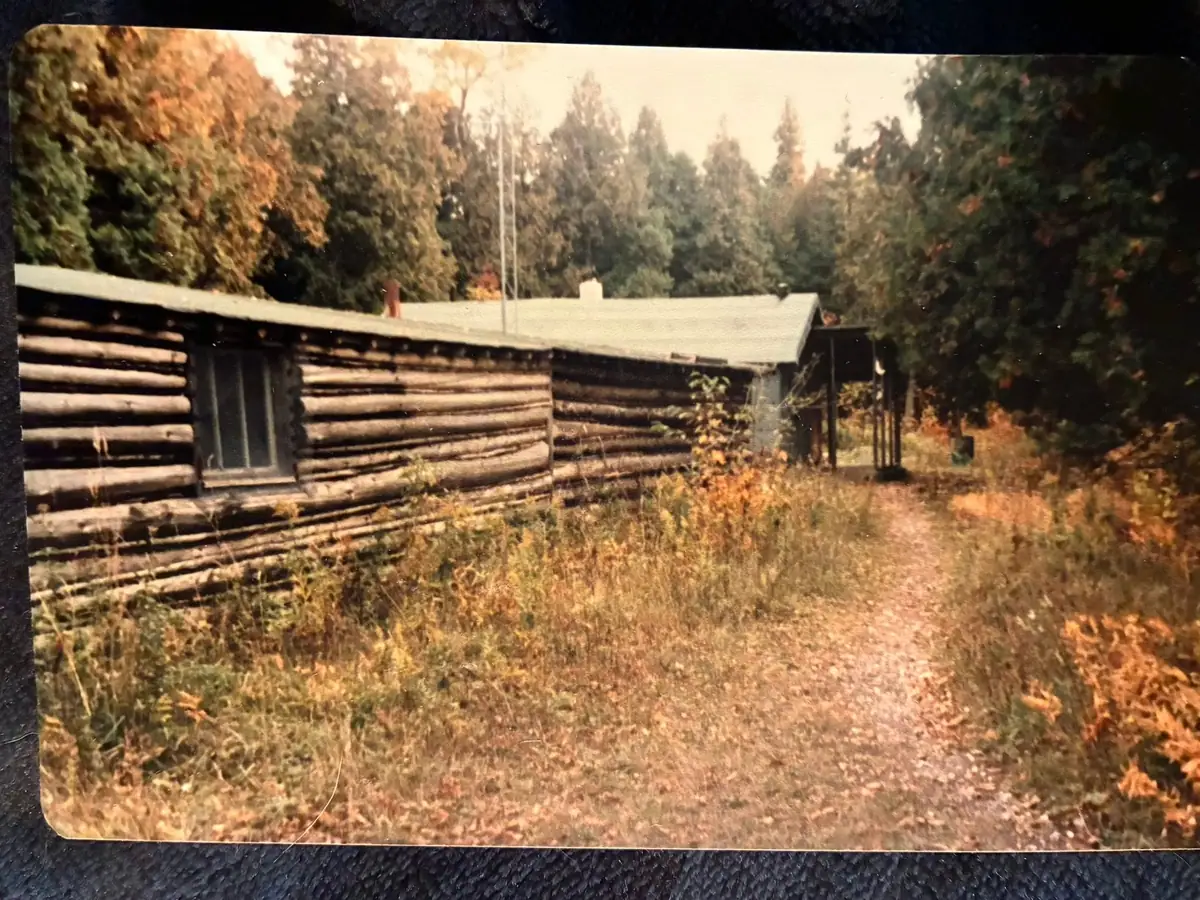 A log cabin beside a narrow path in autumn woods, shown as a physical photographic print.