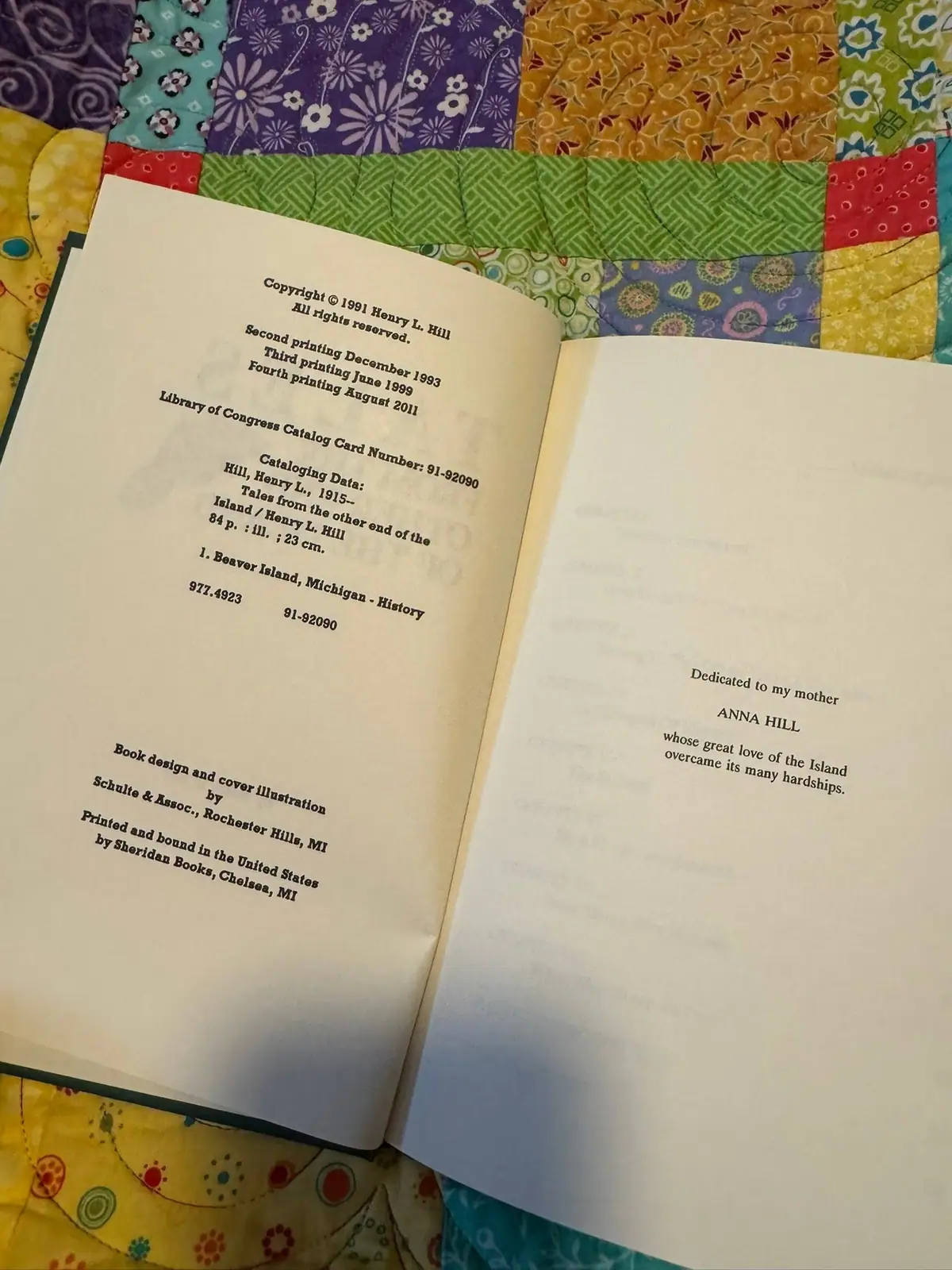 Open book displaying printed cataloging and dedication pages on a colorful patchwork quilt.