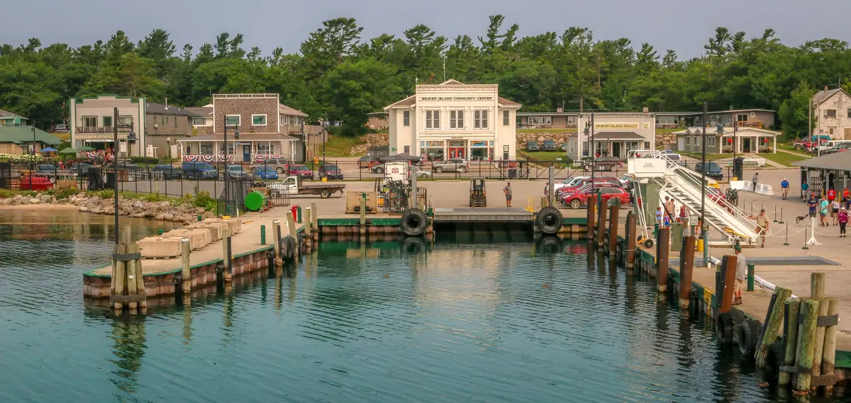 Waterfront landing with docks, a vehicle ramp, buildings, and forested hills behind it.