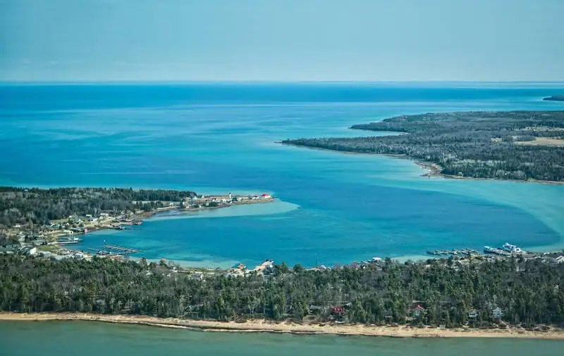 Aerial photograph of a turquoise bay bordered by forest, shoreline homes, docks, and sandy beaches.