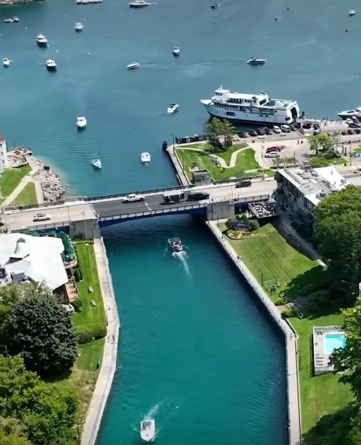Aerial view of a ferry dock, bridge, boats, and a narrow waterway lined with lawns and buildings.