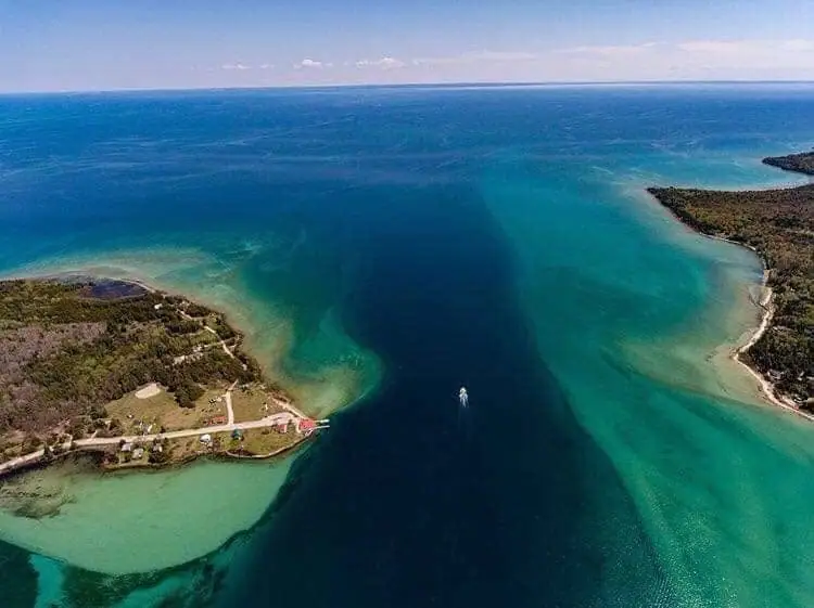 Aerial view of a narrow water channel between wooded shores, with a small boat leaving a wake.