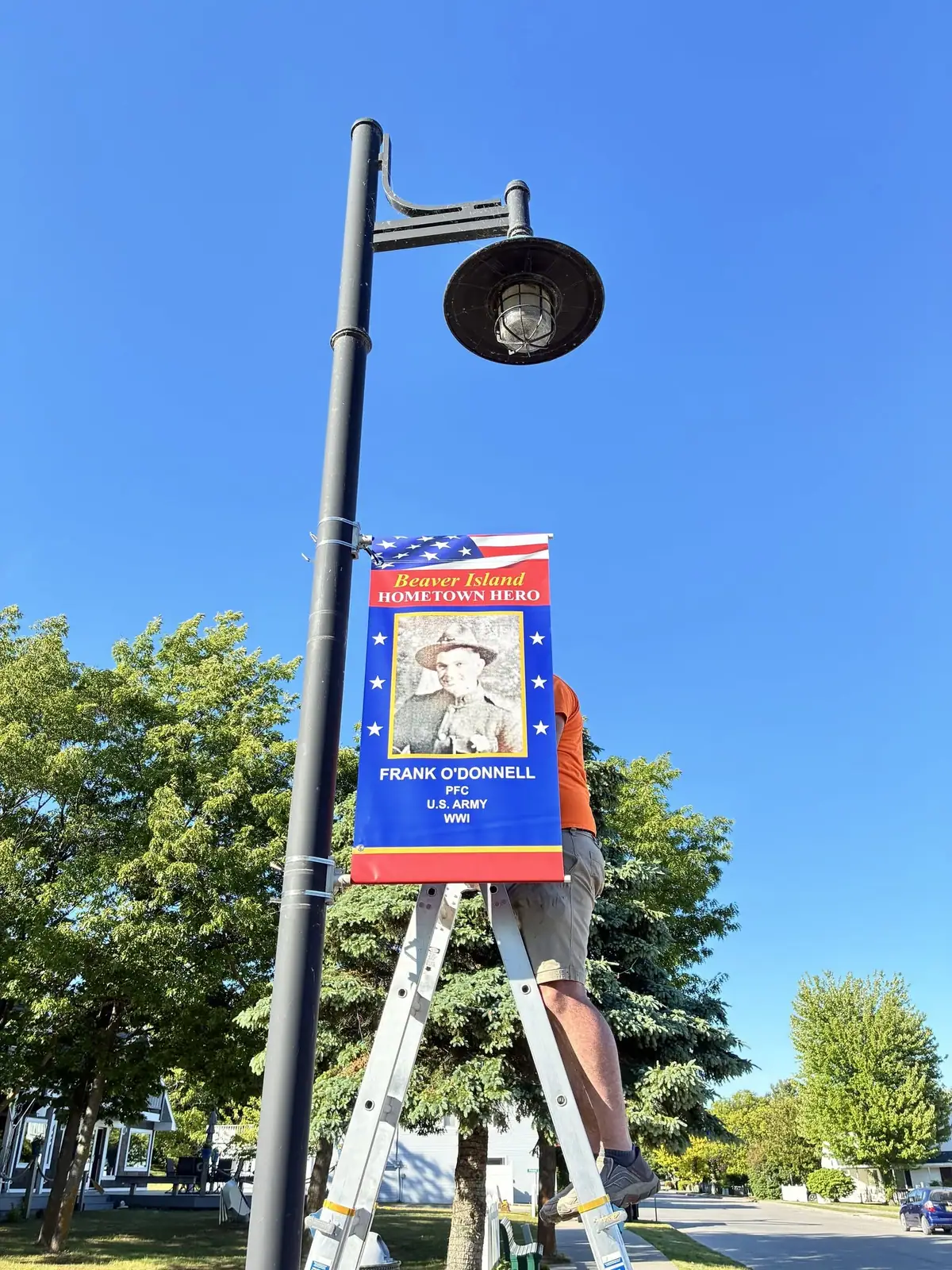 A worker hangs a blue and red World War I hero banner from a black streetlamp.