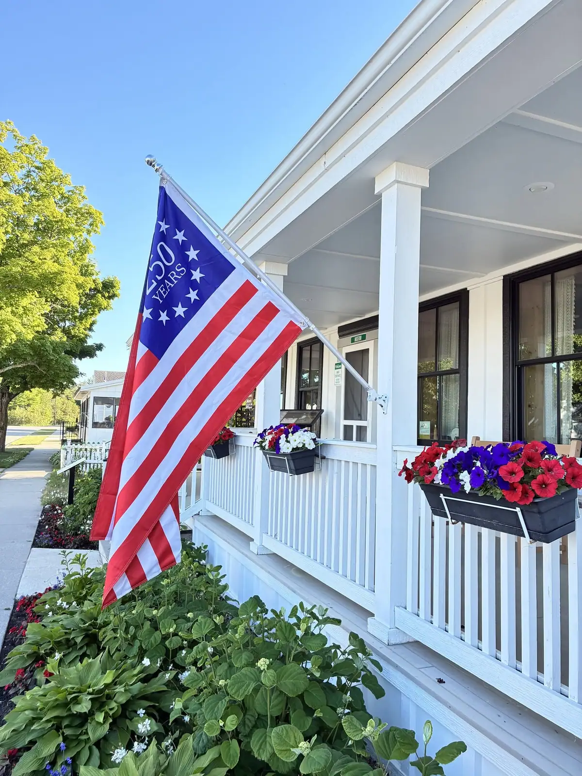 A flower-filled white porch displays an American flag marked “50 YEARS.”