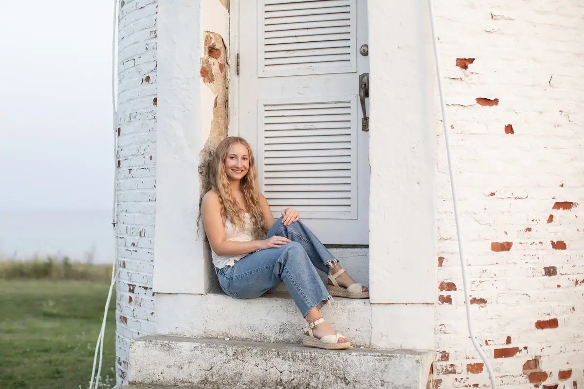 Young woman seated on concrete steps beside a weathered white-painted brick building.