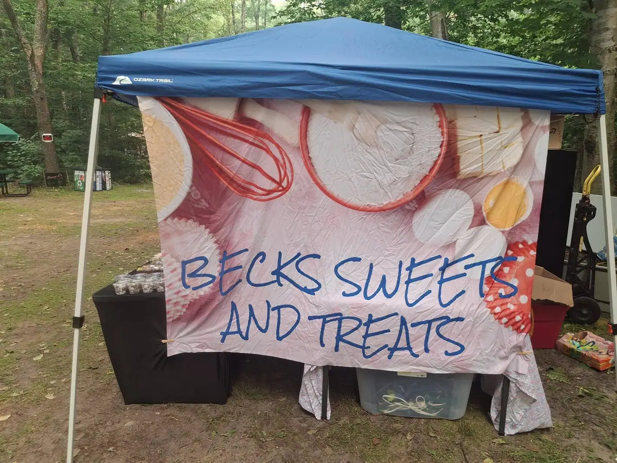 A covered outdoor sweets stall displays treats beneath a hand-lettered banner.