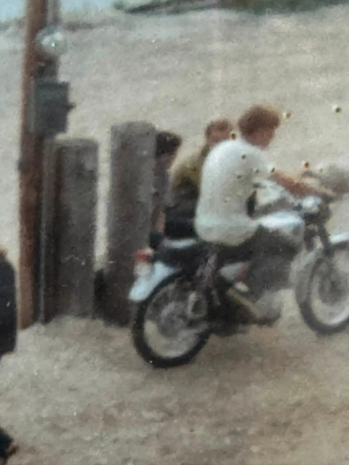 A blurred photograph shows a person seated on a motorcycle beside a building.