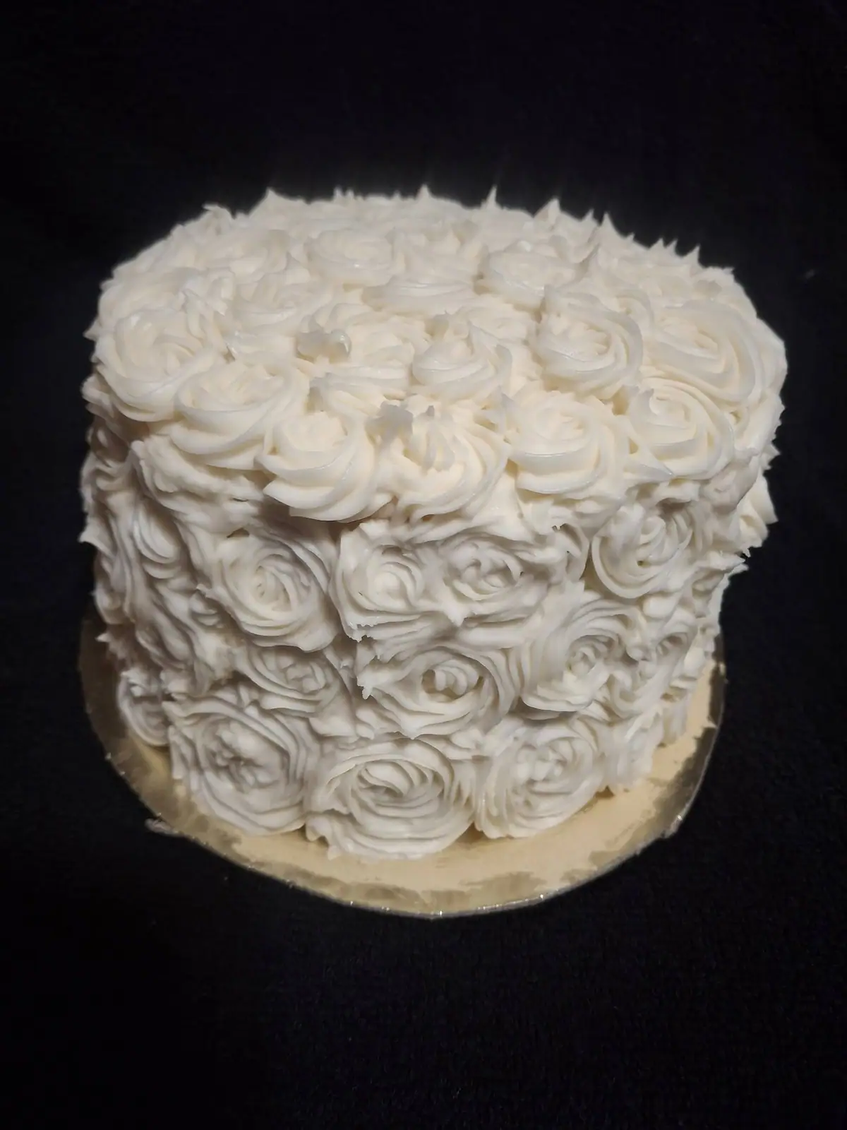 Round cake covered with white piped frosting roses on a gold-colored cake board.