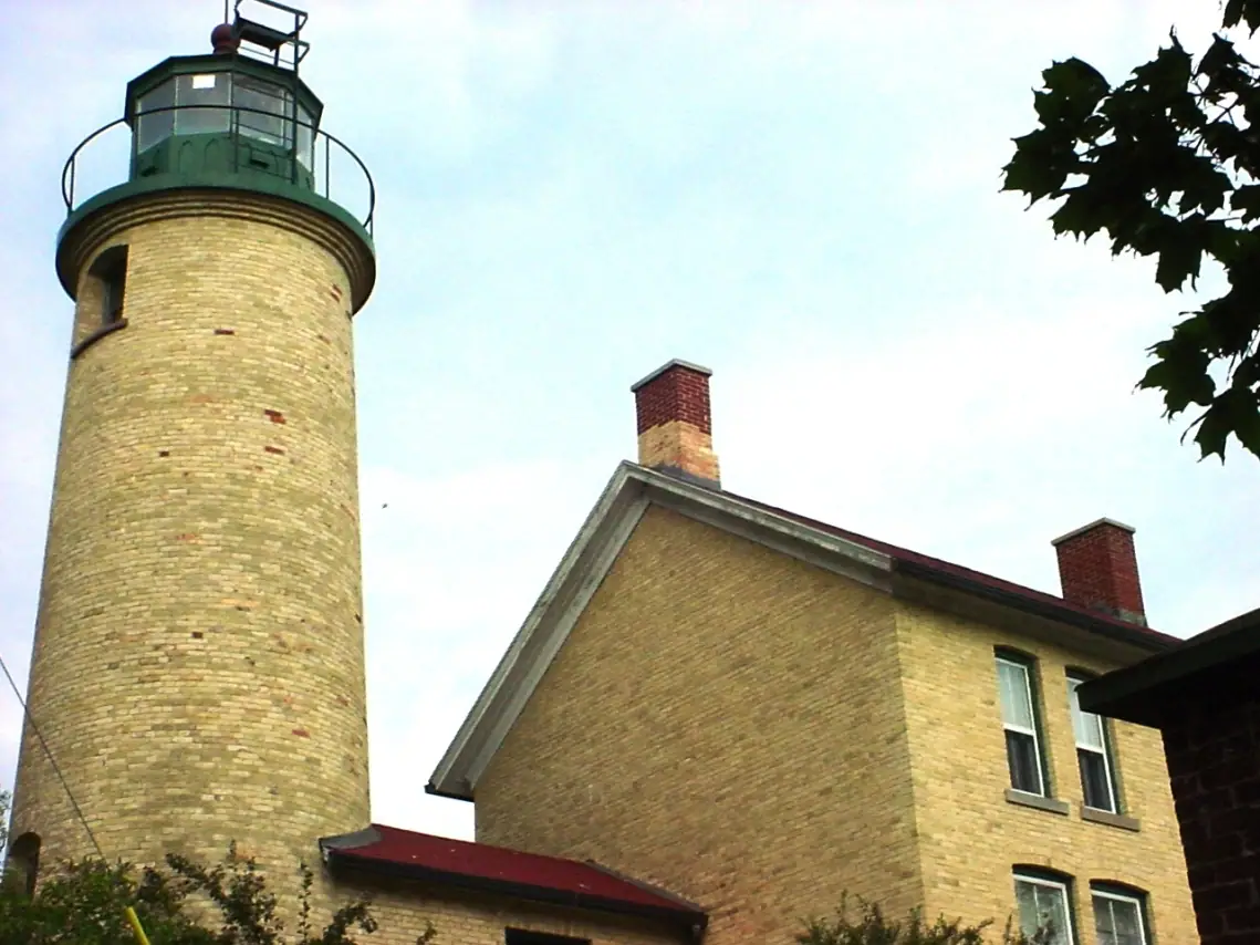 Brick lighthouse tower and adjoining brick building photographed from below.