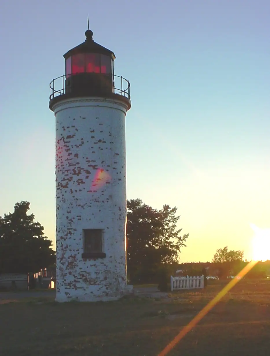 A weathered white cylindrical lighthouse stands against a low golden sun.