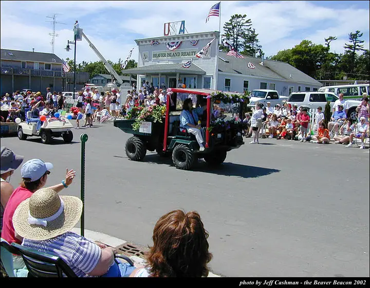 A decorated golf cart passes spectators gathered along a street during a patriotic parade.