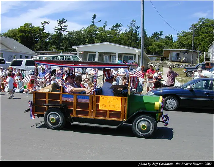 A patriotic parade truck carries people beneath a canopy decorated with flags and bunting.