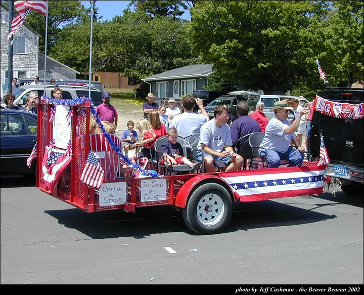 A red patriotic parade float carries adults and children along a residential street.