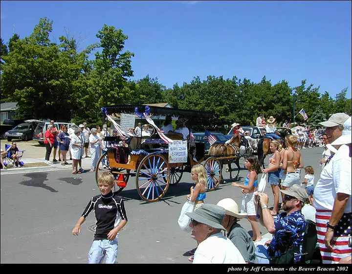 A decorated horse-drawn wagon passes spectators and a child during a street parade.