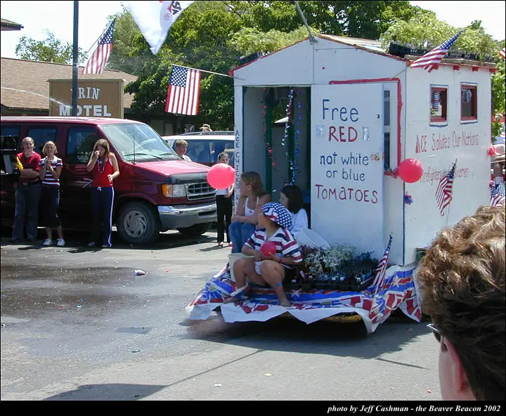 A patriotic parade float decorated with flags, featuring children and a message about red tomatoes.