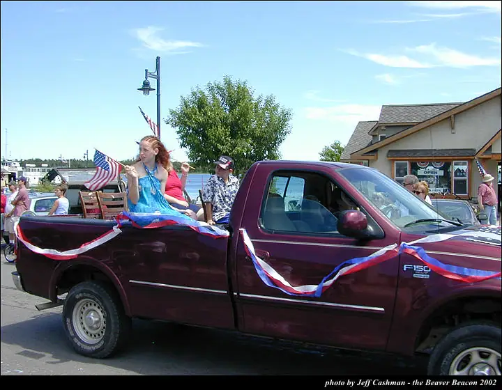 Decorated maroon pickup truck carrying people and an American flag during a street parade.
