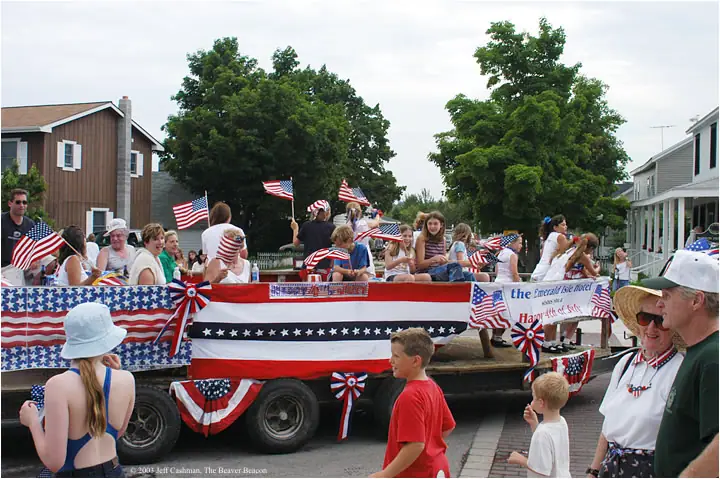 A patriotic parade float carries people and flags along a residential street.
